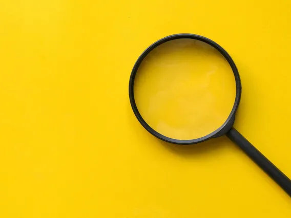 Black magnifying glass on a yellow background.