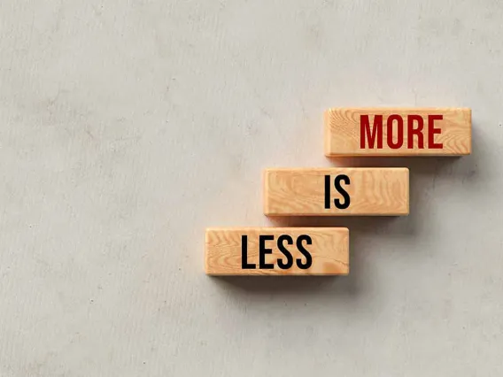 Three wooden rectangles sit on gray background. Each rectangle contains one of the following three words, Less is More.