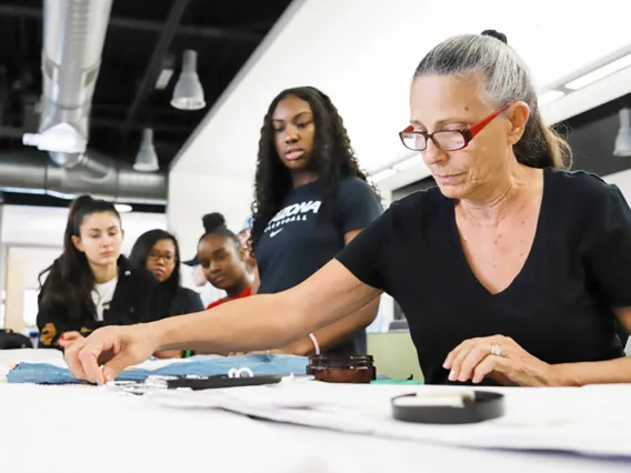 A female textile faculty, demonstrates the gluing of fabrics to other materials to her class. 