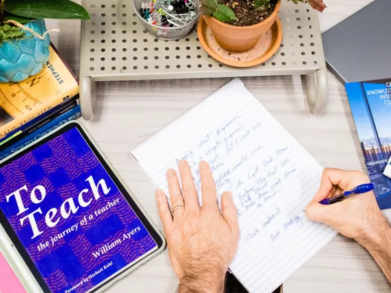  A faculty takes notes for his upcoming class on a paper notepad from a book he read; To Teach, the journey of a teacher by William Ayers.