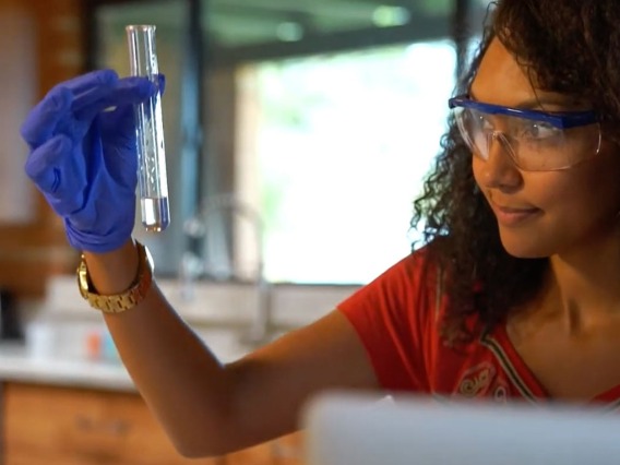 A female student looks at her chemistry test tube while wearing protective eyewear.