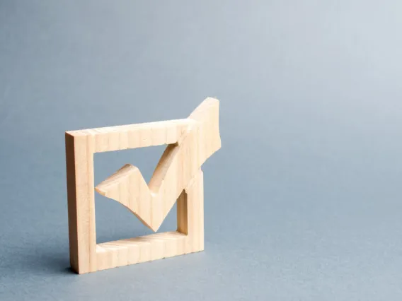 A wooden checkmark sits on a dove blue background.