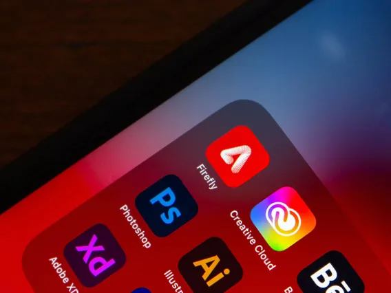 A smartphone interface displays various Adobe Creative Cloud apps, including Firefly, Photoshop, Adobe XD, and Illustrator, among others.