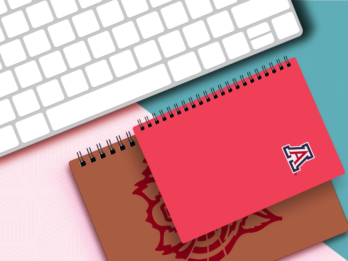A vector-like illustration of two UArizona notepads, one red and one brown, are neatly placed next to a keyboard.
