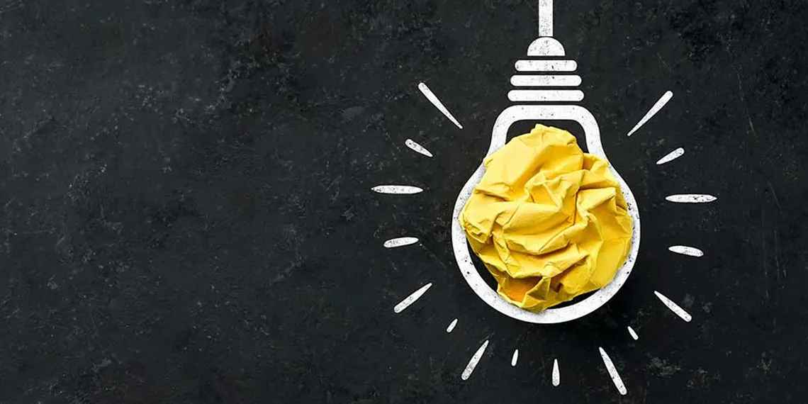 A white painted outline of a lightbulb on a blackboard with a yellow cloth center as a light.
