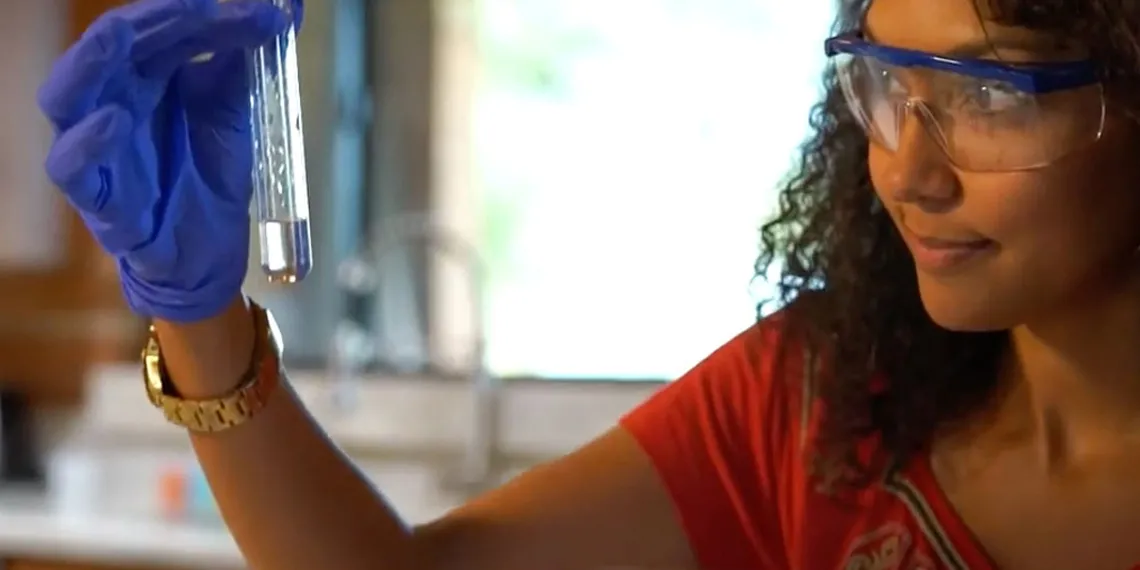 A female student looks at her chemistry test tube while wearing protective eyewear.