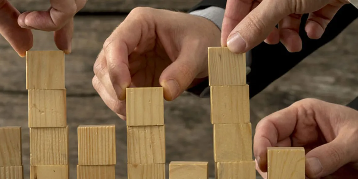 A group of people are arranging a set of wooden cubes on a table.